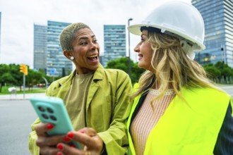 Two diverse colleagues. One an architect wearing a hardhat and safety vest. Looking at a smartphone