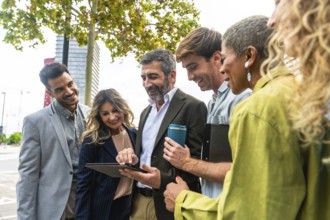 Diverse group of smiling business people looking at a tablet screen together, discussing ideas and