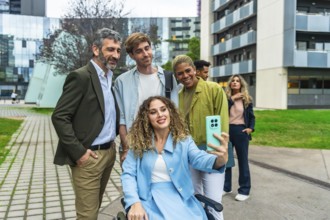 Diverse business team, including a woman in a wheelchair, smiling and taking a cheerful outdoor