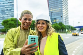 Diverse women architects and engineers smiling outdoors, looking at a smartphone screen,