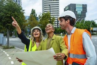 Diverse team of architects and engineers smiling and pointing towards a building, holding