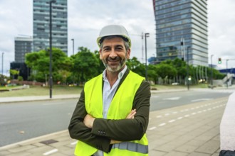 Senior construction professional in hard hat and high visibility vest stands with arms crossed,