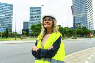 Confident mature professional woman in a hard hat and safety vest standing with crossed arms in a