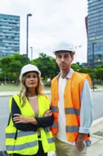 Construction professionals wearing hard hats and reflective vests, standing outdoors, collaborating