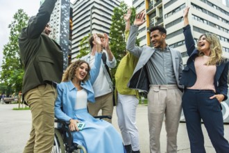 Diverse business colleagues including a woman in a wheelchair cheering and doing high fives