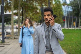 Business colleagues walking on a city sidewalk while communicating on their mobile phones, focusing