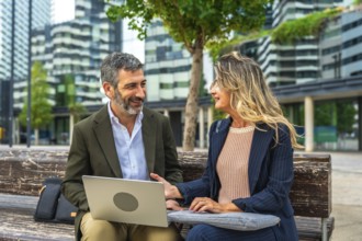 Two smiling business colleagues having an informal outdoor meeting on a bench, collaborating on a