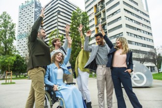 Mixed age businesspeople with a woman in a wheelchair raising their hands in celebration, showing
