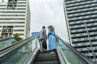 Business professionals ascending an outdoor escalator in a modern urban environment, symbolizing