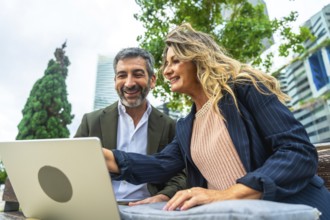 Business colleagues smiling and discussing work outdoors in a park, reviewing information on a