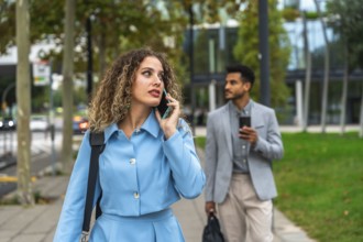 Confident businesswoman talking on her smartphone while walking on a city sidewalk with a male