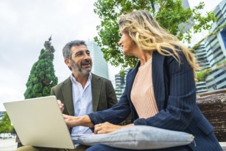 Two business colleagues engaged in a discussion while working on a laptop, sitting together on a