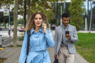 Businesswoman talking on her mobile phone while walking on a city sidewalk with a male colleague