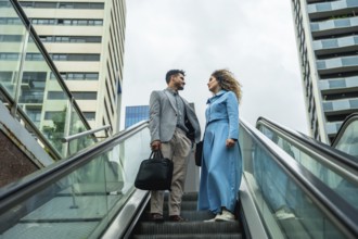 Two business professionals ascending an escalator, engaging in a conversation with modern