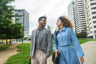 Two diverse business professionals walking along a path in a contemporary urban park with modern