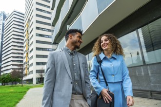 Two diverse business professionals walking outside a modern office building, looking at each other