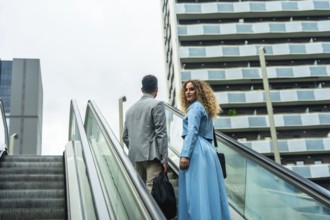 Two diverse business colleagues ascending an escalator, looking towards a modern city building,