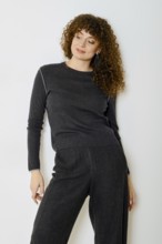 Relaxed woman stands in a cozy dark grey outfit that includes a stylish top and matching pants. The