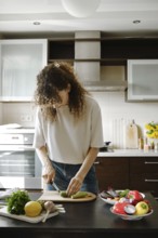Young housewife chopping fresh baby zucchini on wooden board in the kitchen