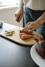 Close-up of female hands chopping fresh baby carrot on cutting board in the kitchen