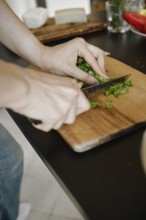 Unrecognizable woman chopping cilantro on wooden cutting board