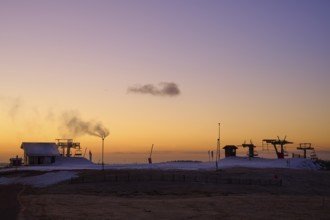 Snow cannons and silhouettes of buildings in evening light against a purple sky, winter, Route de