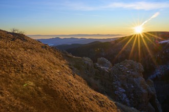 View over a sunlit rock edge in a vast mountain landscape, looking towards the Rhine Valley,