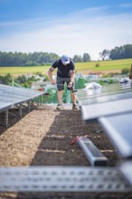 A technical worker installs solar panels on a construction site with a rural background, new Park