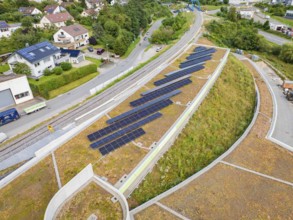 Solar panels on a green hill next to a road and railway line in a residential area, new park and
