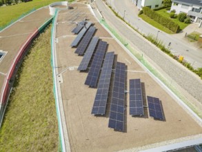 Solar panels on a flat roof next to a street and buildings, surrounded by green vegetation, new