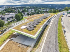 Building with solar system on green roof next to railroad tracks in a cloudy landscape, new park