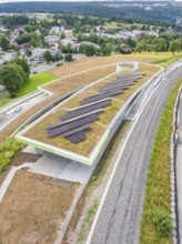 Solar panels on a covered building next to a railway line, surrounded by countryside, new park and