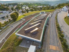 A large roof with solar panels, along a road in a green landscape, new park and ride parking garage