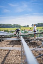 Two men install solar panels on a construction site surrounded by rural fields, new Park and Ride