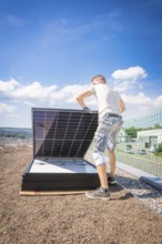 Person installs solar modules on a structure under a blue sky, new park and ride parking garage