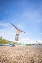 Person carrying a solar panel on a construction site with blue skies and nature, new park and ride
