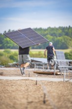 Workers install solar panels with cables in an open field under a blue sky, new park and ride