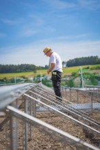 A construction worker stands on scaffolding in a rural area under blue skies, new park and ride