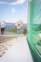 Worker carrying a solar panel on a construction site with a view of the mountains, new Park and