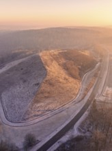 Snowy hill in sunset light with surrounding roads, old deposit, construction site for PV open space