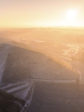 Snow-covered hilltop in soft orange light of morning sun, old deposit, construction site for PV