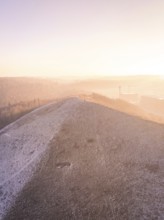 Hill covered by snow at sunrise with light fog, old deposit, construction site for PV open space