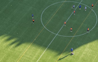 Players wearing colorful jerseys play soccer on a grass field from a bird's eye view from the tower
