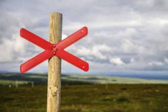 Red snowmobile snowscooter marker on a wooden post in front of a vast landscape under clouds,