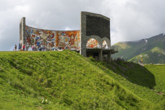 Grassy hill with painted wall, people enjoying the view, Georgian-Russian Friendship Memorial,
