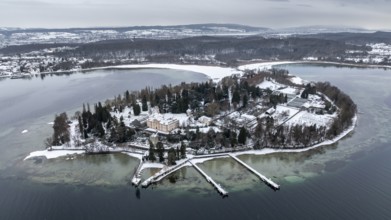 The wintry and snowy Mainau island in Lake Constance with the pier and the baroque Mainau Castle,
