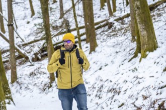 Man in yellow beanie and green jacket with backpack walking through snowy woodland, enjoying a