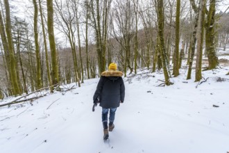 Person walking uphill in a winter forest, carrying a camera, wearing warm clothing with a yellow