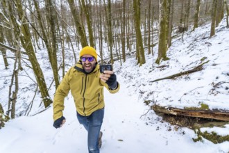 Happy man in a yellow beanie and green jacket smiling at his action camera while vlogging on a
