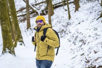Adult male adventurer, wearing a yellow beanie, yellow jacket, sunglasses, and backpack, walking